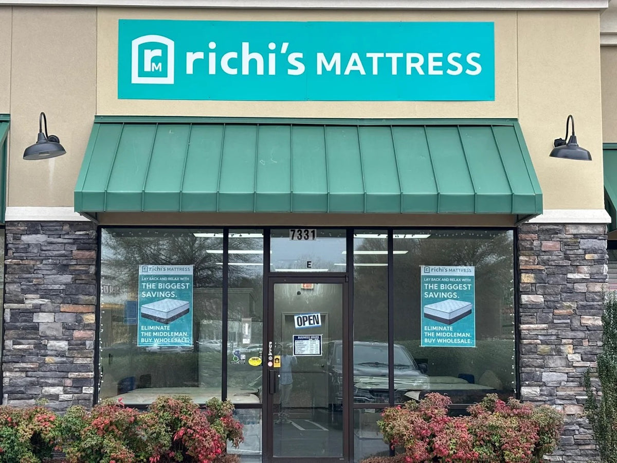 Front exterior of Richi's Mattress store with a teal sign above the entrance, green awning, stone veneer walls, glass doors, and storefront windows.